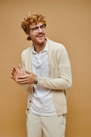 overjoyed redhead man in old money style attire looking away and laughing on beige backdrop