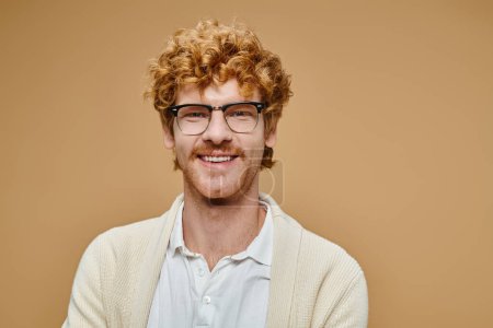 portrait of cheerful redhead man in eyeglasses and trendy light-colored clothes on beige backdrop