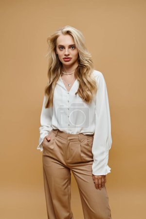 femme blonde confiante vêtements à la mode posant avec la main dans la poche sur beige, vieille mode de style argent
