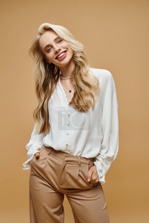 fröhliche blonde Frau in trendiger Freizeitkleidung posiert mit den Händen in den Taschen auf beiger, klassischer Mode