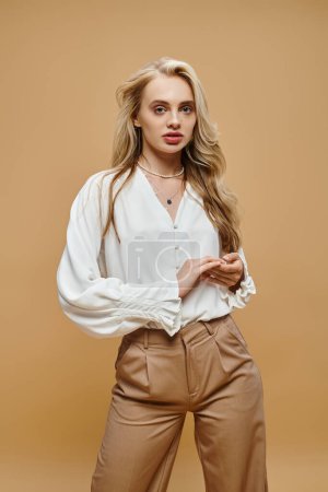 Téléchargez les photos : Jeune femme blonde dans un style classique vêtements décontractés regardant la caméra sur beige, mode intemporelle - en image libre de droit