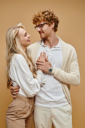 young stylish couple embracing and looking at each other on beige backdrop, old money style fashion