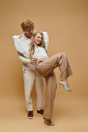 joyful and trendy couple in old money style clothes having fun on beige backdrop, full length