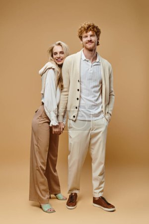 Foto de Longitud completa de feliz pareja joven en ropa casual de moda cogidas de la mano mirando a la cámara en beige - Imagen libre de derechos