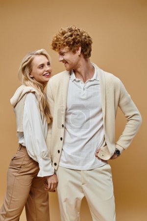 Téléchargez les photos : Jeune et insouciant couple dans des vêtements de couleur claire à la mode en se regardant sur beige - en image libre de droit