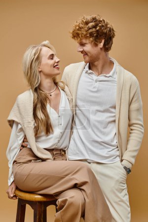 elegant blonde woman and redhead man smiling at each other on beige backdrop, old fashion style