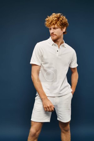 redhead male model in white trendy clothes posing with hand in pocket on blue, old money style