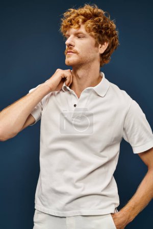 fashionable redhead man in white attire with hand in pocket looking away on blue, classic fashion