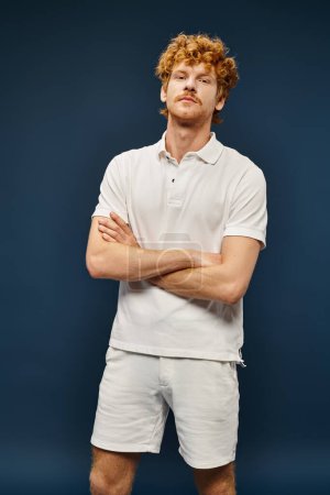 confident redhead man in white stylish clothes with folded arms on blue, old money style fashion