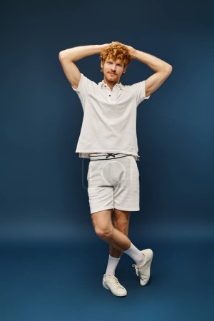full length of aristocratic man in white polo t-shirt and shorts with hands behind head on blue