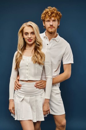 young elegant couple in old money style clothes looking at camera on blue backdrop, timeless fashion