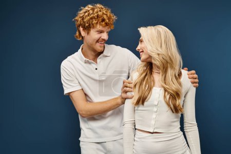 glückliches und wohlhabendes Paar im weißen Outfit, das sich auf blauer, alter Geld-Mode anschaut