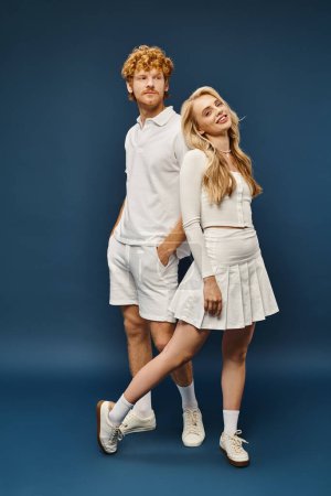 volle Länge des aristokratischen Paares in weißen stilvollen Kleidern Rücken an Rücken auf blauer, klassischer Mode