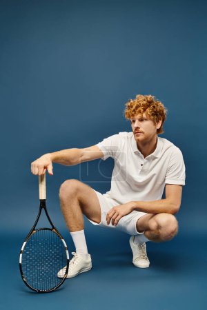 Téléchargez les photos : Homme rousse à la mode en tenue de tennis blanc assis sur des hanches avec raquette sur bleu, vieux style d'argent - en image libre de droit