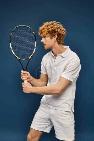 active aristocratic redhead man in white trendy clothes playing tennis on blue, classic fashion