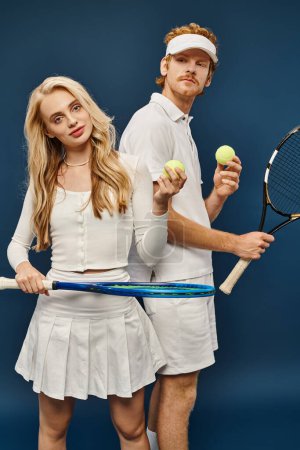 Photo for Aristocratic young couple in white attire with tennis racquets and balls on blue, old money fashion - Royalty Free Image
