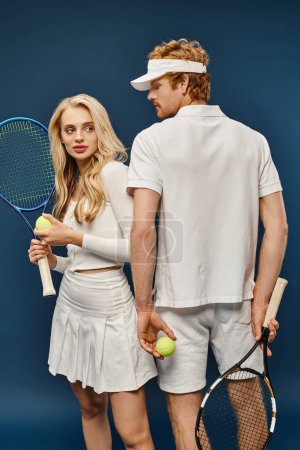 jeune couple branché en tenue de tennis blanche avec raquettes et balles sur bleu, vieux style argent