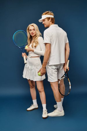 Photo for Full length of young couple in white tennis attire with racquets and balls on blue, old money style - Royalty Free Image