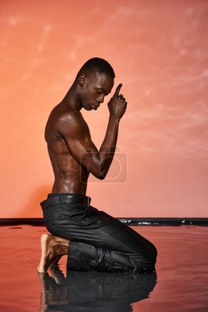 attraktive afrikanisch-amerikanische Mann in schwarzen nassen Hosen sitzt auf dem Wasser, umgeben von lebendigen Lichtern