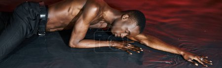 Foto de Atractivo hombre afroamericano en pantalones mojados acostado en la superficie del agua con los ojos cerrados, luces, pancarta - Imagen libre de derechos