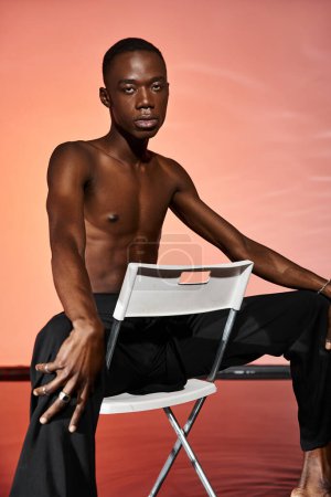handsome sexy african american man sitting shirtless on chair and looking at camera, red lights