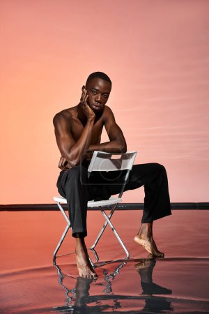 attractive sexy african american man sitting shirtless on chair and looking at camera, red lights