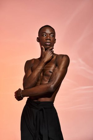 sexy african american man standing shirtless in black pants surrounded by lights and looking away