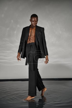 Téléchargez les photos : Charmant homme afro-américain élégant en costume déboutonné sexy posant sur fond gris aqueux - en image libre de droit