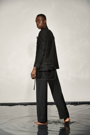 appealing african american man in black sexy suit posing attractively on gray watery background