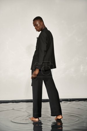 Téléchargez les photos : Beau homme afro-américain en costume noir élégant posant alléchamment sur fond aqueux - en image libre de droit