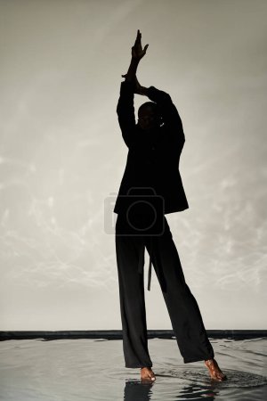 silhouette of stylish african american man posing barefoot in suit on watery backdrop in shadows
