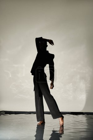 Silhouette eines stylischen afrikanisch-amerikanischen Mannes, der barfuß im Anzug auf wässrigem Hintergrund im Schatten posiert