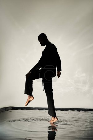 silhouette de charmant homme afro-américain posant pieds nus en costume sur fond aqueux dans les ombres