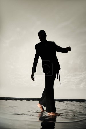 silhouette de charmant homme afro-américain posant pieds nus en costume sur fond aqueux dans les ombres