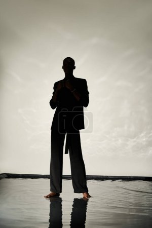 silhouette of charming african american man posing barefoot in suit on watery backdrop in shadows