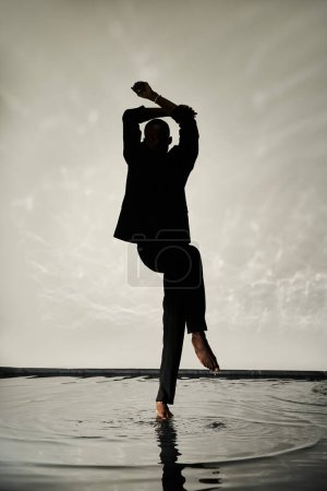 silhouette of tempting african american man posing barefoot in suit on watery backdrop in shadows