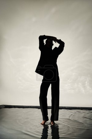 silueta del tentador hombre afroamericano posando descalzo de traje sobre fondo acuoso en las sombras