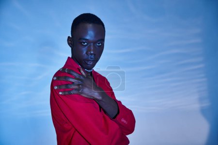 good looking young african american man in red vibrant blazer posing on blue watery background