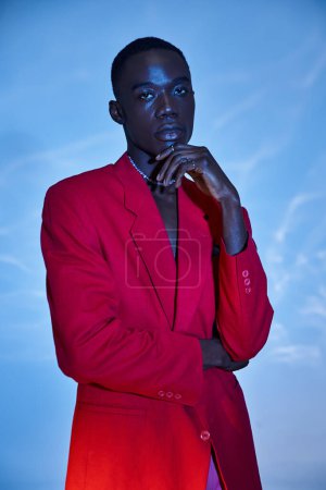 Téléchargez les photos : Attrayant jeune homme afro-américain en rouge vibrant blazer posant sur fond bleu aqueux - en image libre de droit