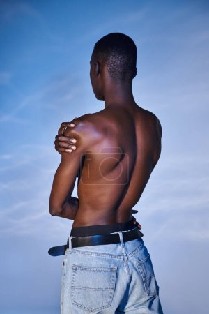 back view of fashionable shirtless african american man in stylish jeans on blue watery backdrop