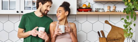attractive jolly diverse couple in homewear enjoying hot coffee and looking at each other, banner