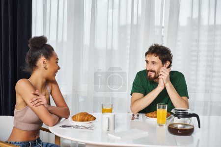 Téléchargez les photos : Séduisant beau couple interracial en tenues décontractées profiter de leur délicieux petit déjeuner à la maison - en image libre de droit