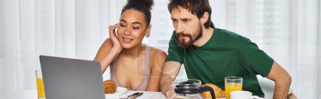 Téléchargez les photos : Attrayant couple multiculturel joyeux en vêtements de maison regarder des films pendant le petit déjeuner, bannière - en image libre de droit