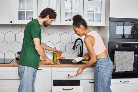 fröhlich gut aussehendes vielseitiges Paar in gemütlicher Hauskleidung, das nach dem Frühstück seine Küche putzt