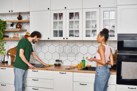 ansprechende freudige interrassische Paar in Homewear Hausarbeit und Putzen Küche nach dem Frühstück