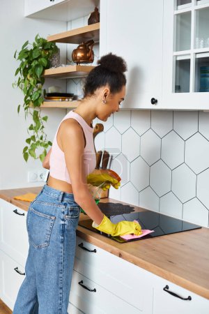 beautiful cheerful african american woman in cozy homewear washing her stove during spring cleaning