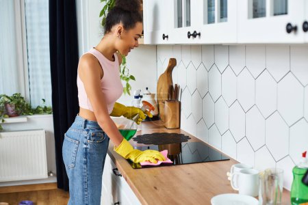 appealing african american woman in casual attire washing stove using rag during spring cleaning