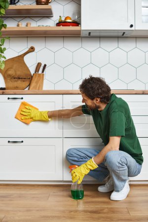 good looking jolly man in casual outfit using rag and cleanser to wash counter, spring cleaning