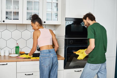 lustige schöne interrassische Paar in Homewear reinigen ihre Geschirr aufmerksam zu Hause