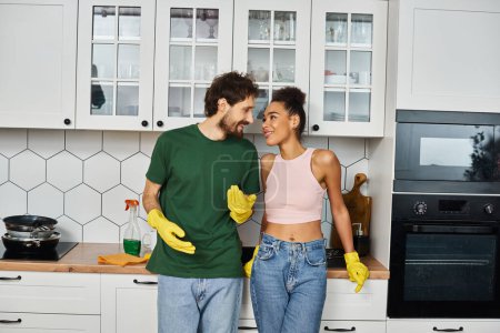 appealing multicultural jolly couple in casual attires smiling at each other during spring cleaning